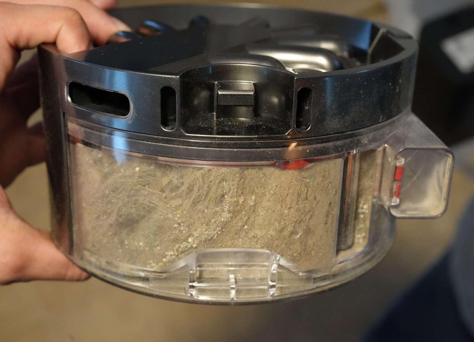 Felix holding the Dyson 360 Vis Nav dust bin packed with cat hair, litter, and dust
