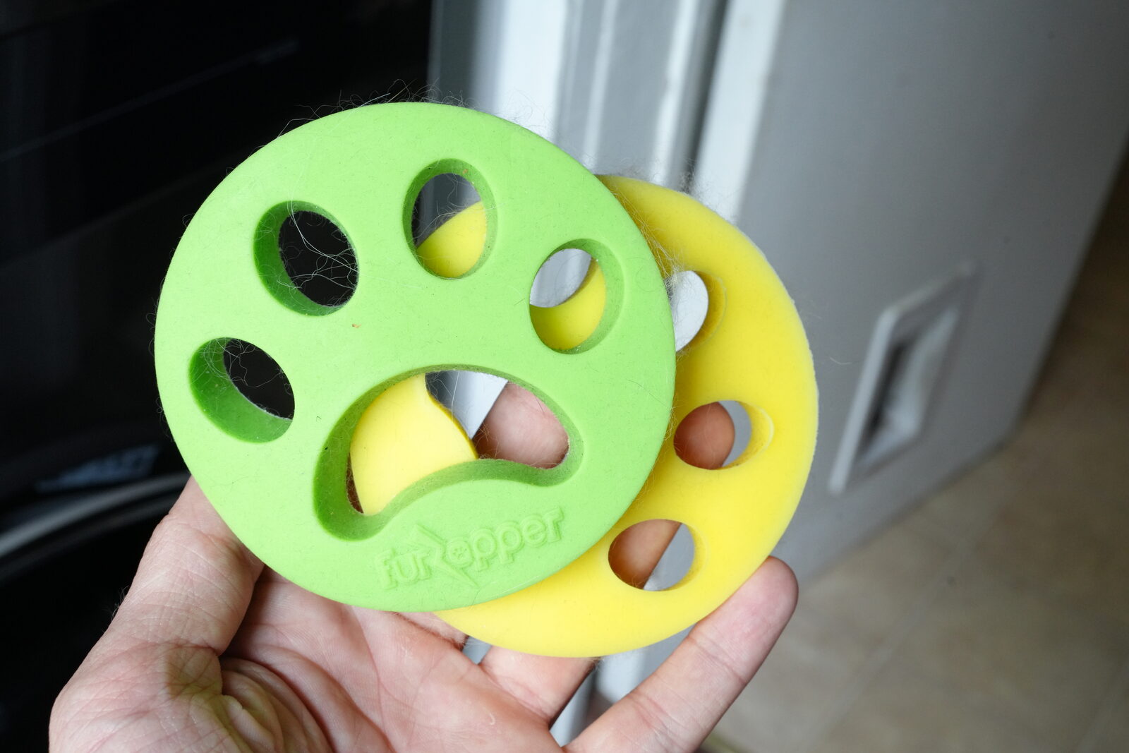 Two FurZapper silicone laundry discs, paw-shaped, with cat hair caught in their cutouts